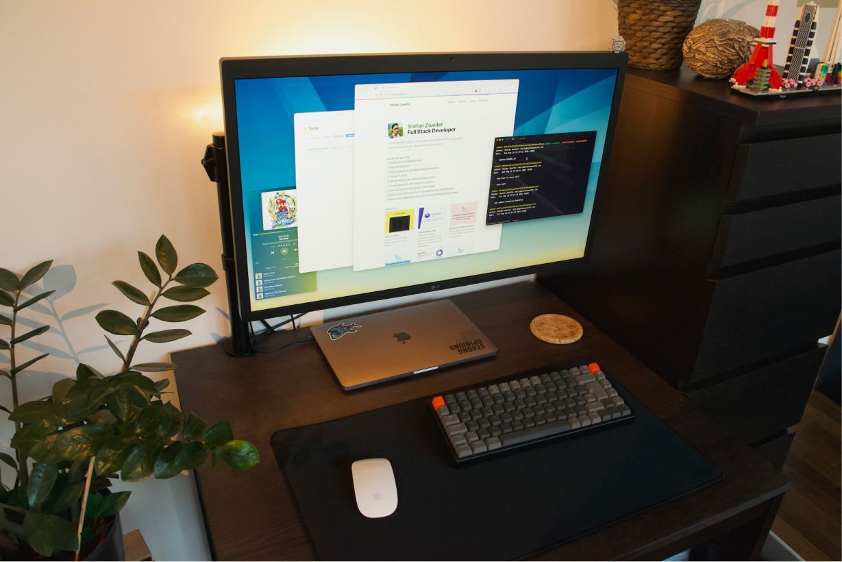 A brown desk on which a MacBook Pro, an LG Ultrafine display and a Keychron mechinal keyboard is placed.