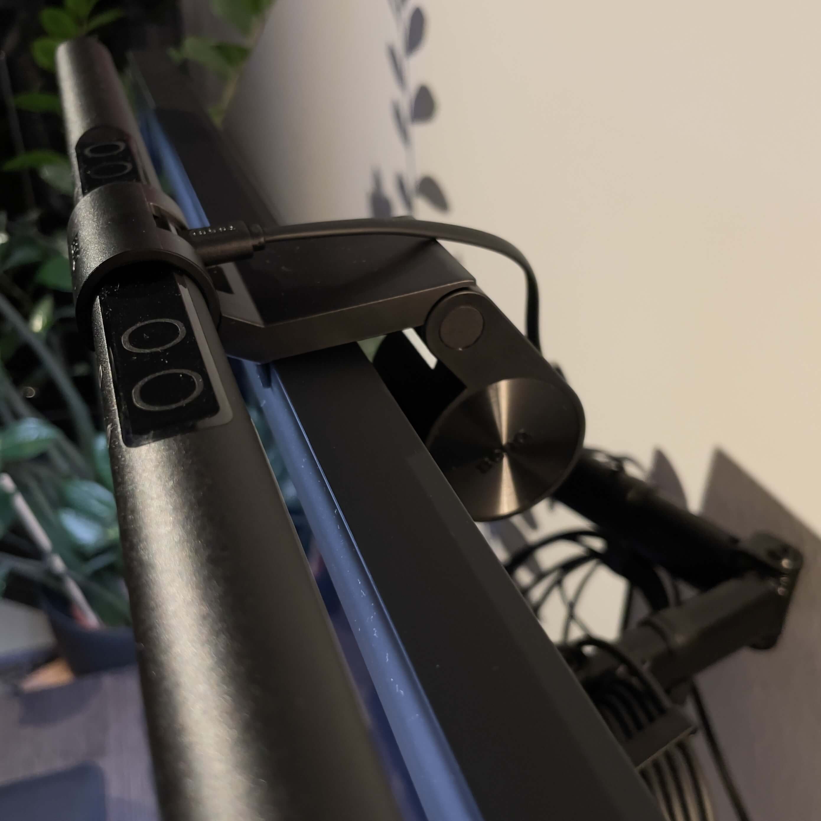 Photo showing the lamp resting on a monitor. The photo is taken from aboth, so to see how the counterweight rests on the back side of the monitor. Other cables are also shown on the photograph. A couple of green leaves can be seen in the background.